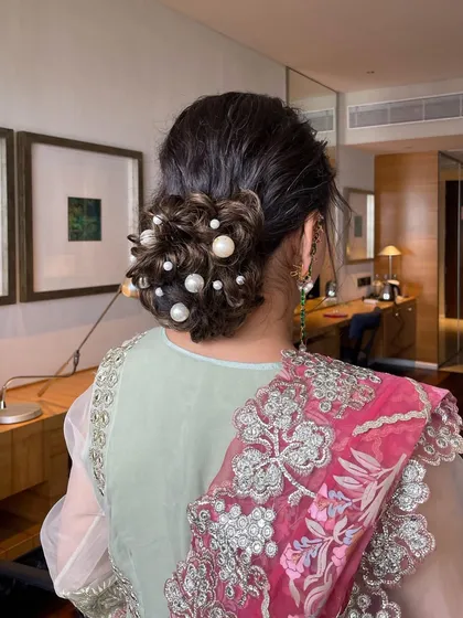 A messy bun decorated with dispersed pearls of various sizes. This is a modern and chic take on a classic updo, perfect for a cocktail party or reception.