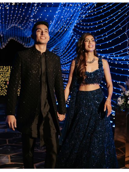 The couple makes a grand entrance, walking hand-in-hand under a canopy of twinkling fairy lights, setting a magical tone for their Sangeet night.