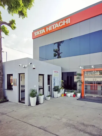 A look at the completed Tata Hitachi dealership in Faridabad. The design features a clean, modern exterior with a seamless rainscreen system and bold brand colors, establishing a strong corporate identity while integrating harmoniously with the surrounding environment.