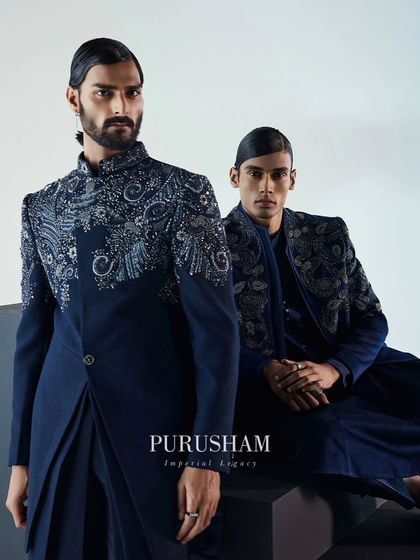 Another portrait of the navy blue velvet ensembles. The asymmetrical cut of the jacket on the left contrasts with the more traditional silhouette on the right, both united by exquisite silver embroidery.