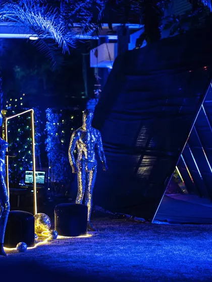 A futuristic party entrance with shimmering mannequins and a mirrored triangular tunnel, setting a high-energy, modern tone.