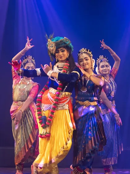 A captivating group formation from "KRISHNA", with the central dancer portraying the divine flute player surrounded by his devotees. The lighting and costumes create a rich visual tapestry.