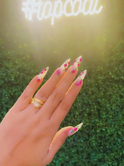Turning nails into masterpieces is my passion. This photo, taken against our salon's backdrop, showcases a beautiful hand-painted floral design on sharp stiletto nails.