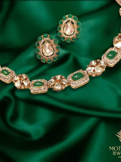 A stunning necklace and earring set featuring uncut Polki diamonds and vibrant green emeralds, laid against a rich green silk.