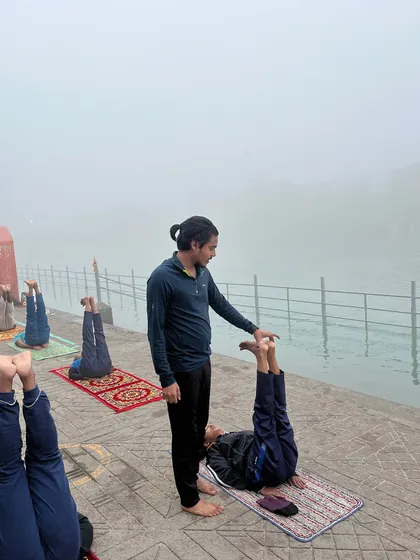 Offering support and encouragement to a student holding an inversion by the Ganges.