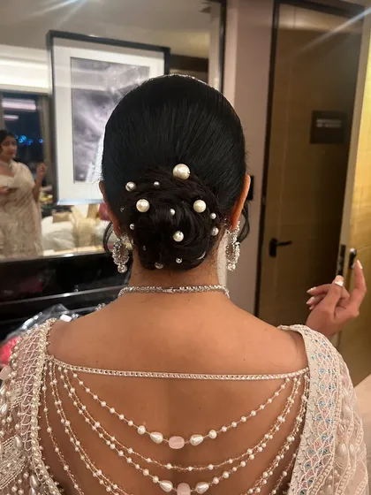 Classy, timeless, and elegant. This sleek bun is adorned with pearls of various sizes, perfectly complementing the pearl detailing on the back of the blouse.