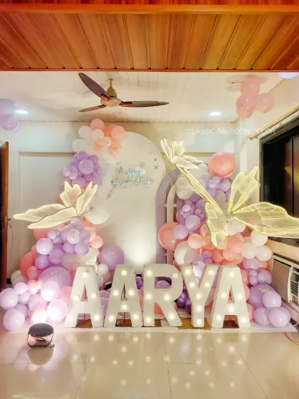 For baby Aarya's first birthday, we created this magical butterfly-themed photo corner. The setup features large marquee letters for the name, soft pastel balloon garlands, and beautiful illuminated butterfly wings.