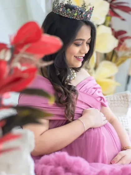 A soft and gentle portrait. The mom-to-be is framed by red flowers in our studio, wearing a lovely pink gown and a crown, capturing a moment of quiet joy.