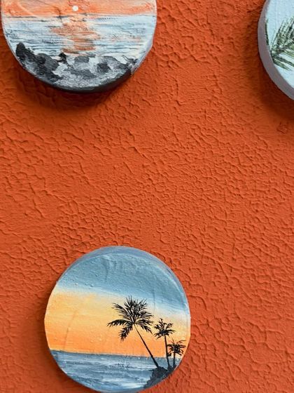 A detailed view of two miniatures, one showing a rocky beach at sunset and another with palm trees. The texture of the acrylic paint adds depth to these small scenes.