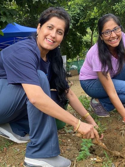Two smiling volunteers from NTT Data work together to plant a native sapling, helping to enrich the biodiversity of the Aravali Creek.