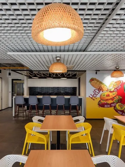 This cafe features vibrant murals depicting classic Mumbai street food like "Cutting Chai" and "Hot Dogs". The use of wicker pendant lights and colorful chairs creates a fun, eclectic atmosphere.