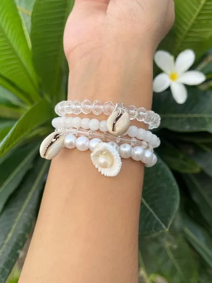 For a beachy, bohemian vibe, this white and shell-themed bracelet stack is perfect. It features clear beads, pearls, and natural cowrie shells for a beautiful, summery look.