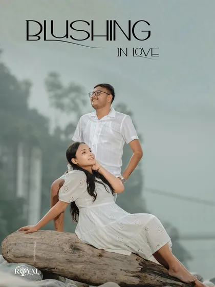 A serene portrait of a couple in all-white outfits relaxing on a log by the river, titled 'Blushing in Love'.