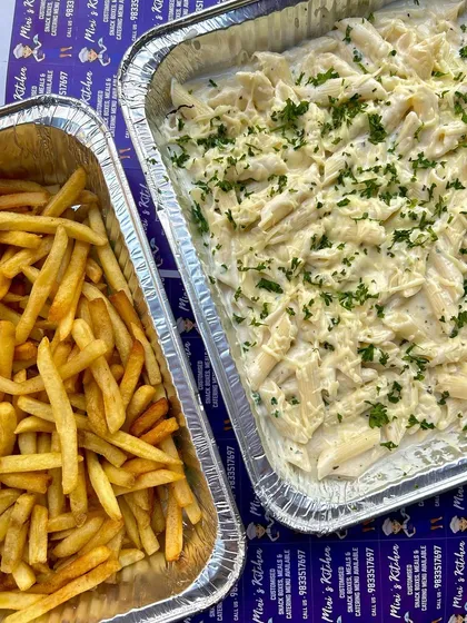 A party-sized tray of cheesy white sauce pasta next to a tray of crispy french fries. A classic combination for any casual gathering.