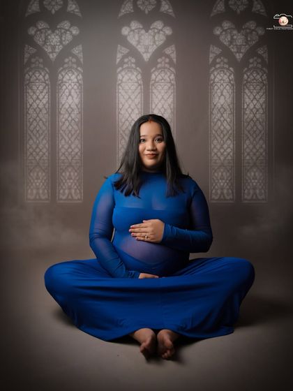 A serene, seated yoga pose where the mother-to-be cradles her bump. Her direct gaze and calm smile create a powerful connection with the viewer, radiating peace and confidence.