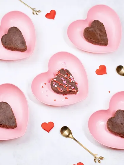 A flat lay of heart-shaped brownies on pink heart-shaped plates. This creative and thematic setup is perfect for seasonal campaigns like Valentine's Day.