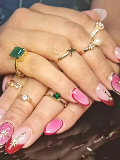 A whimsical and colorful design with pink and red nails, accented with gold starburst charms, rhinestones, and delicate outlines.