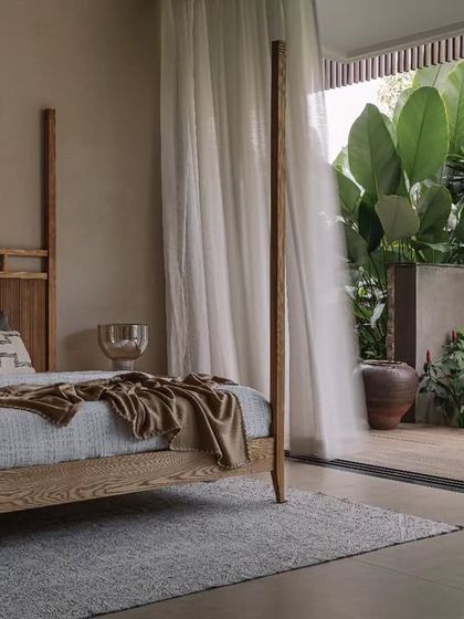 The guest bedroom, with its simple four-poster bed and neutral linens, looks out onto the lush garden. The space is designed to be a peaceful retreat for visitors.