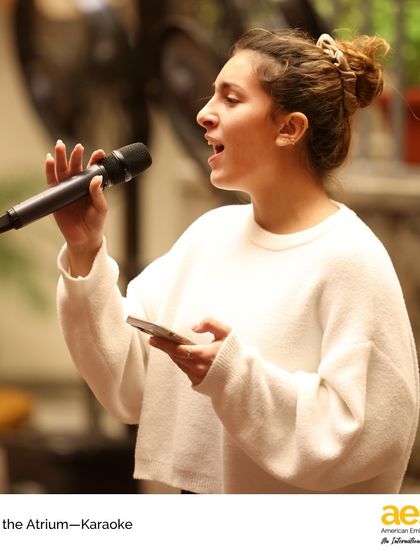 A student confidently performs a solo at karaoke night. Events like this help build public speaking skills and stage presence in a fun, low-stakes environment.