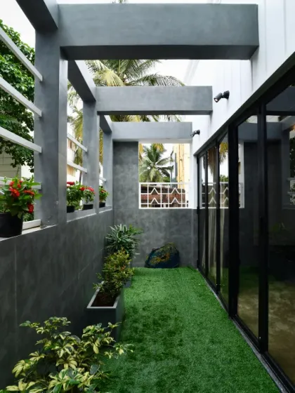 A narrow side courtyard is transformed into a green corridor with artificial turf and potted plants. The design uses vertical space and contrasting textures of concrete and greenery to make the most of a compact area.