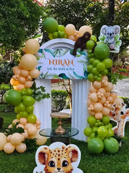 We transformed this garden into a wild jungle adventure for a first birthday. The setup includes an organic balloon arch in earthy tones, a custom 'Into the Wild at One' backdrop, and adorable cutouts of jungle animals like lions, monkeys, and giraffes.