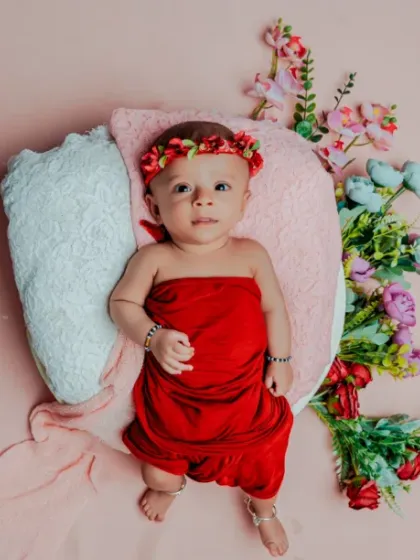 A happy three-month milestone. This baby is wide awake and looking right at the camera, surrounded by red and pink props.