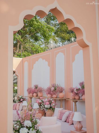 A view through a hand-painted arch reveals a cozy lounge area filled with an abundance of pink flowers and soft textiles.