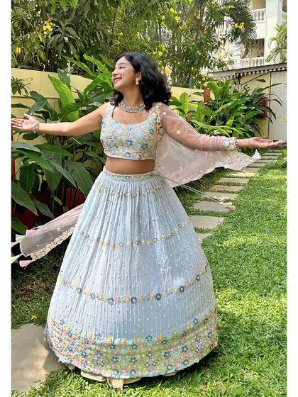 The client twirling joyfully in a garden, showing off the beautiful movement and embroidery of the light blue lehenga.
