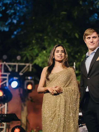 A candid moment from a client's cocktail event. The groom looks sharp in a classic black suit, a timeless choice that perfectly complements his bride's shimmering gold saree.