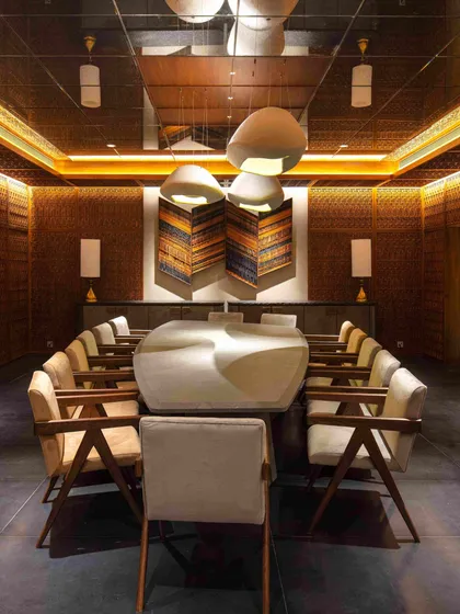 For the Bammi Residence's basement dining room, we transformed a space without natural light into an opulent, jewel-box-like chamber. The walls and ceiling are enveloped in intricate Pinjirakari-inspired lattice work, a traditional craft that creates a warm, filtered glow. The bespoke dining table and curated art pieces complete this immersive and atmospheric dining experience.