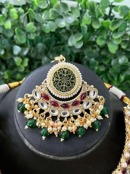 A close-up of a maang tikka that is part of a larger set, showing intricate green and red details.