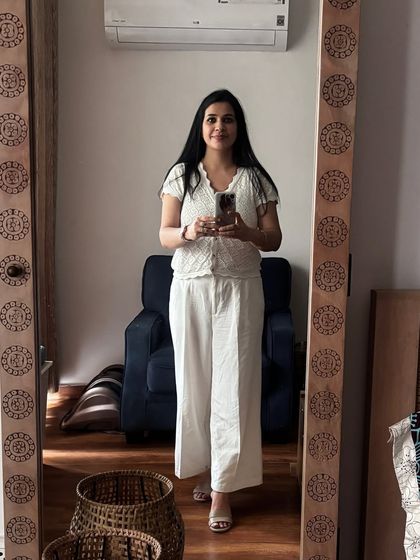 A mirror selfie showing a simple and chic all-white outfit. I've paired a crochet top with wide-leg white trousers for a comfortable and elegant summer look.