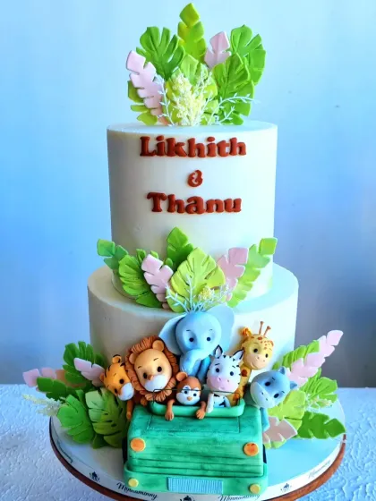A straight-on view of the two-tiered safari wedding cake, showing the cute animal toppers and tropical leaves.