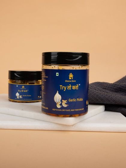 A styled shot of Garlic Pickle jars on a marble board with a dark napkin, giving it a gourmet presentation.