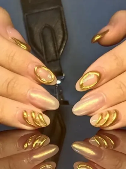 A showcase of avant-garde nail design, featuring a sheer pearlescent base with bold, 3D sculpted gold accents that create texture and architectural interest.