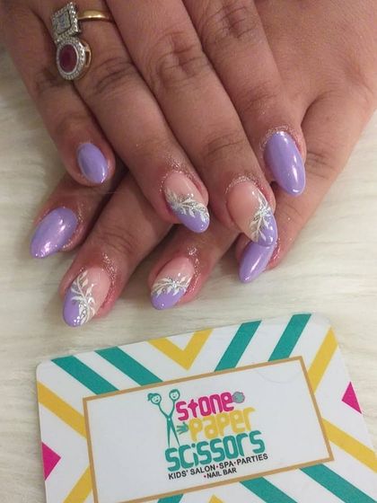 A lovely combination of solid lavender nails and accent nails with a delicate, hand-painted white leaf design over a nude base. This is a soft and elegant nail art option.