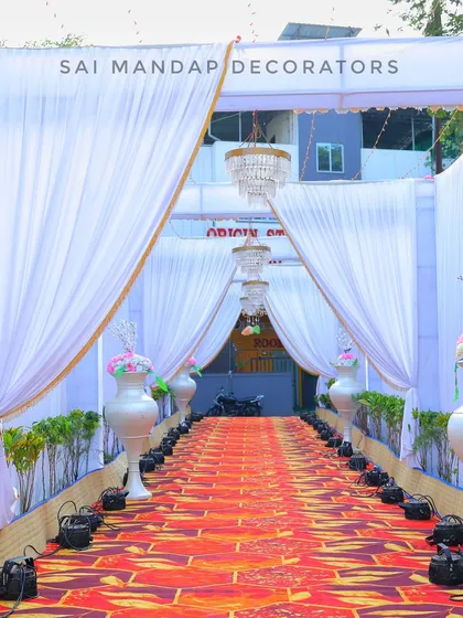 This view shows the long, decorated walkway leading from the entrance. The path is lined with traditional vases and spotlights, all under a canopy of white fabric and sparkling chandeliers.