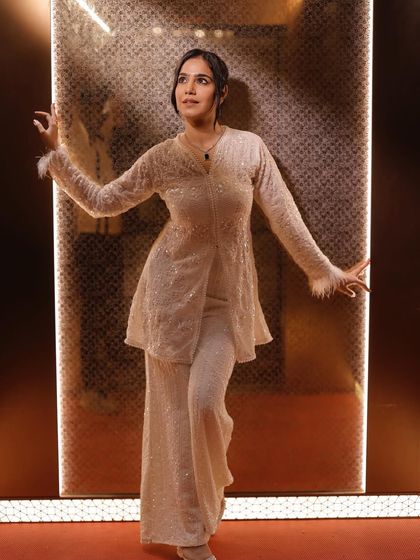 A confident pose in the same white outfit, highlighting the feather details on the sleeves.
