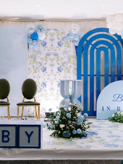 Feeling the baby blues with this gorgeous 'Baby in Bloom' shower. The decor features shades of blue with floral-patterned and slatted backdrops, large 'BABY' blocks, and elegant balloon and flower arrangements.