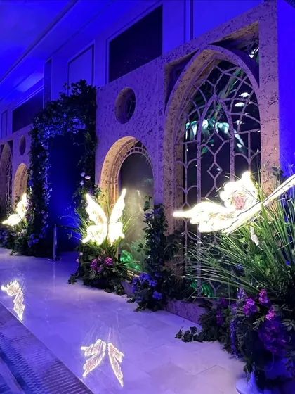 Archways lit up with whimsical butterflies and a bed of wild blooms. We use creative lighting and unique props to turn simple walkways into magical experiences. 💜🦋