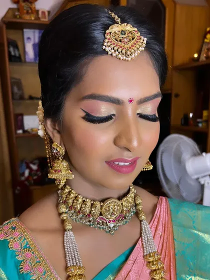 This close-up shows the soft shimmer on the eyelids and the sharp winged liner that defines the eyes. The makeup is subtle enough to let her natural beauty and her exquisite temple jewellery shine.