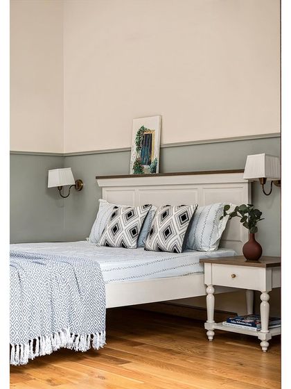 The bed in the parents' room features a classic paneled headboard. The wall is color-blocked with a muted sage green on the bottom half, adding character to the space.