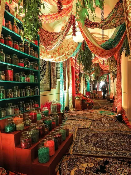An immersive entrance designed to look like a bustling bazaar, with colorful carpets, draped fabrics, and shelves of spices and glitter, creating a unique and memorable guest experience.