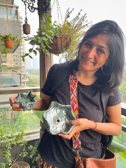A student proudly holding her two unique, flower-like bowls, fresh from the kiln with a beautiful green glaze.