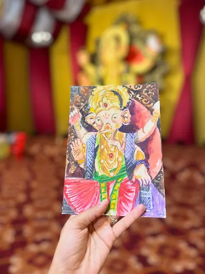 Holding up my finished watercolour of the Ganpati idol at the Bal Vikas pandal. The blurred background of the actual pandal makes the colours of my painting stand out.