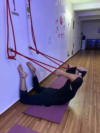 An advanced student works on a prone backbend using the wall ropes for leverage.
