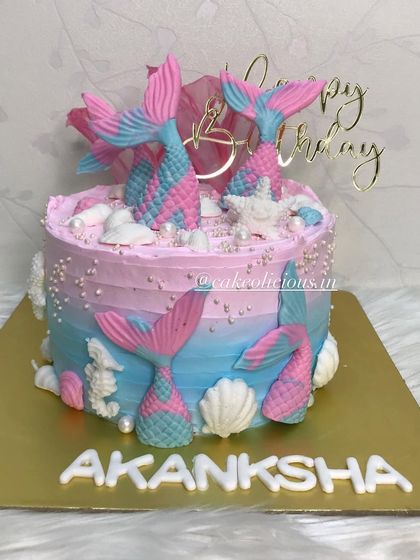 A mermaid beauty for a birthday. This whipped cream cake features pink and blue ombre frosting, decorated with shimmery mermaid tails and seashells.