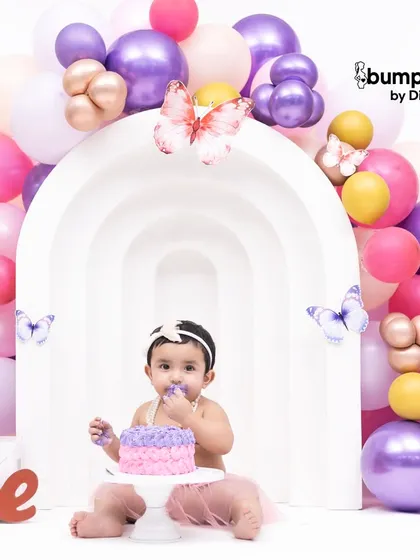 A wider view of the butterfly themed cake smash, showing the beautiful balloon arch and the happy birthday girl enjoying her cake.