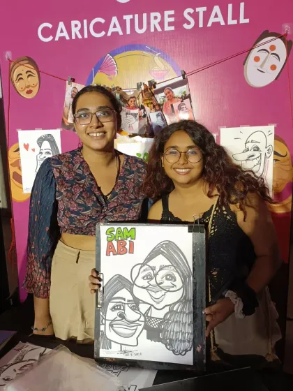 Two friends posing with their group caricature in front of our stall.