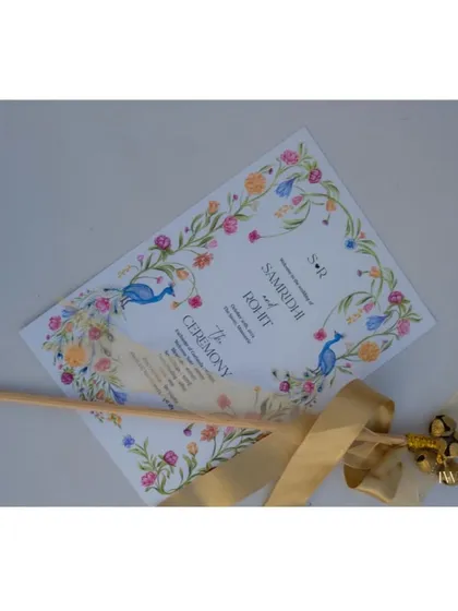 A beautifully designed ceremony program for a wedding in the hills. The custom watercolor illustration of peacocks and florals, paired with a ribbon-tied bell, served as a lovely and practical keepsake for guests.